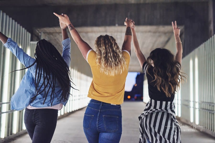 three confident young women walking together holding hands in the air