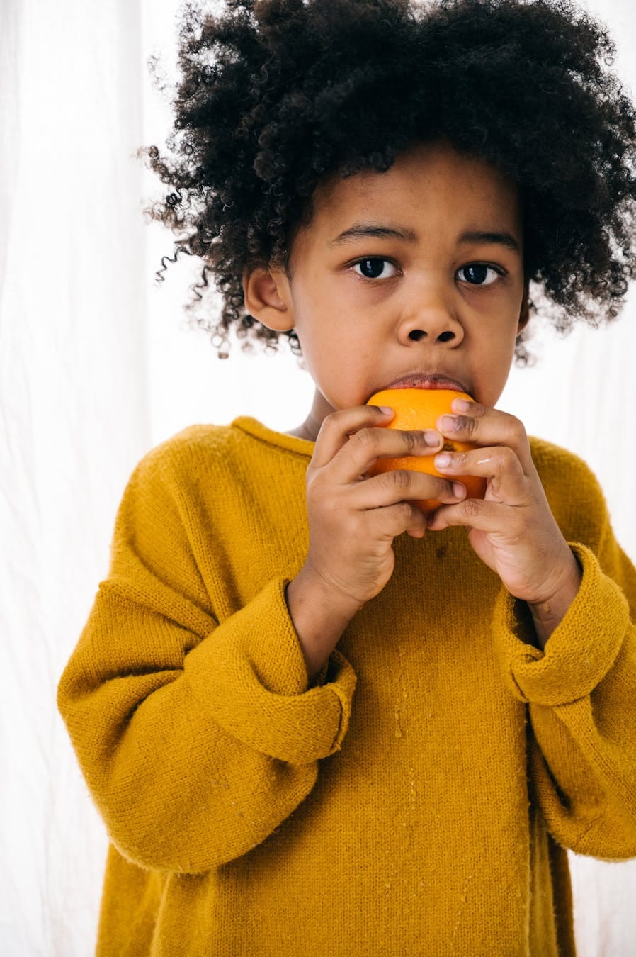 Young child enjoying a fresh orange indoors, showcasing healthy eating and nutrition.