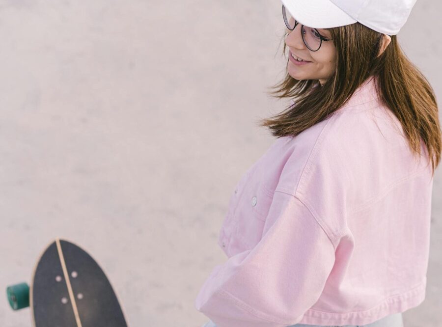 Young woman in casual attire with a longboard in an outdoor setting, showing an active lifestyle.