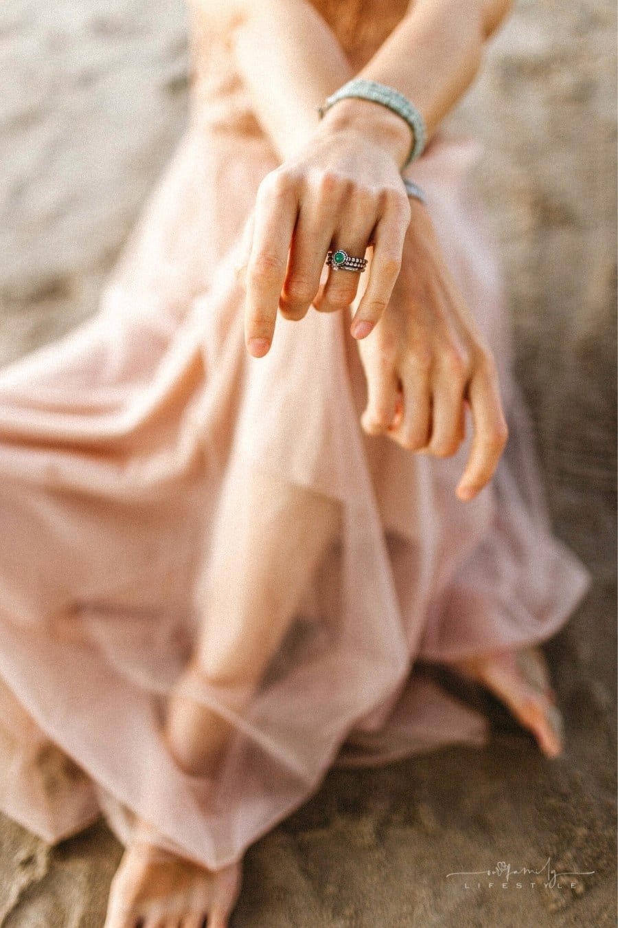 woman wearing pink flowing dress and silver jewelry sitting on a beach