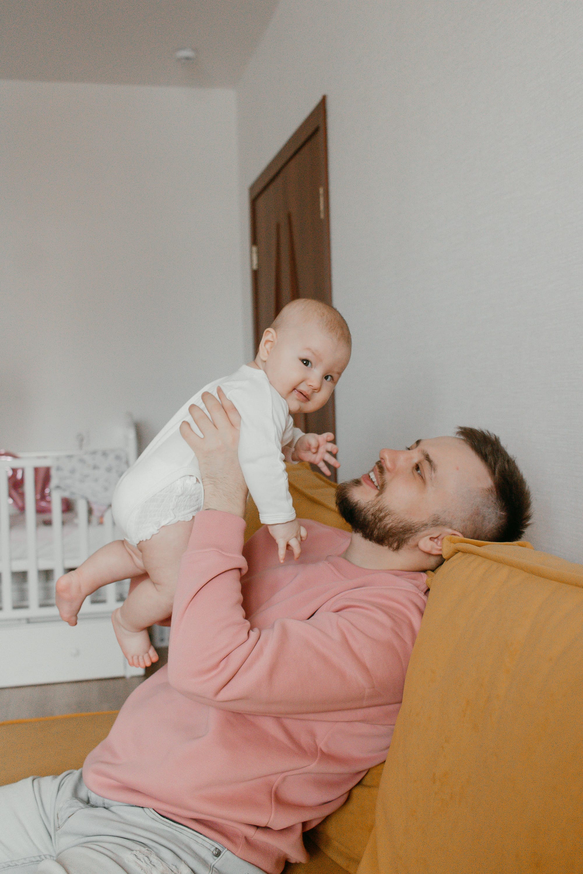 Man in Pink Sweater Holding Baby in Hands