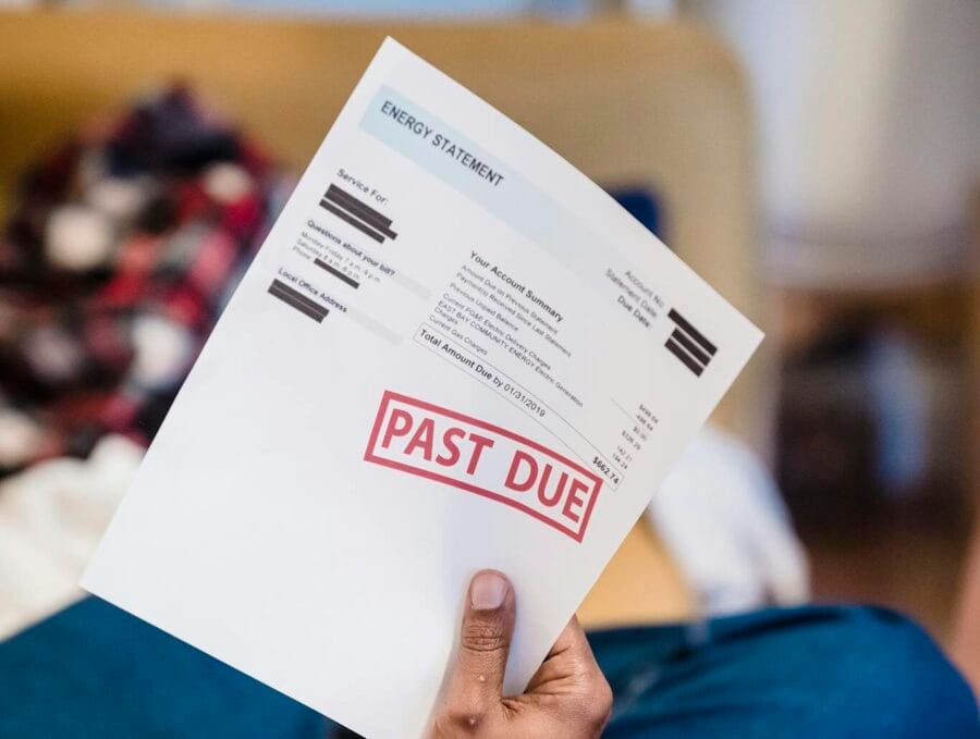 A man holding a past due billing statement while lounging indoors, expressing financial stress.