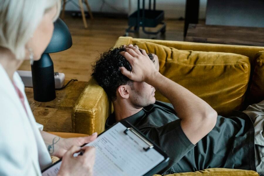 A man lying on a sofa during a therapy session, appearing distressed.