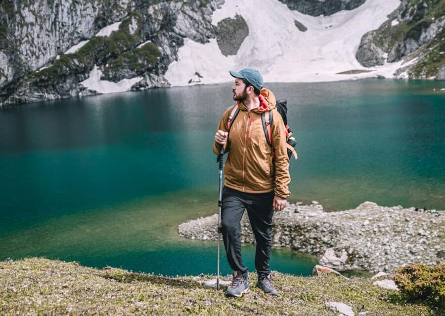 A man stands by a pristine mountain lake surrounded by snow-capped peaks, depicting a serene travel moment.