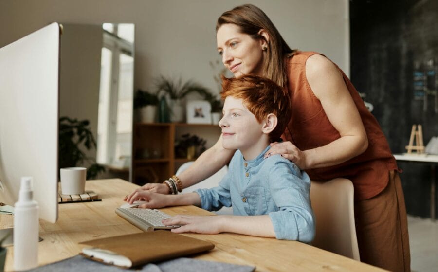 A mother and her child smiling while using a computer at home, focused on learning.