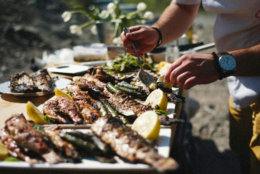 A vibrant outdoor barbecue with grilled fish and fresh lemons being prepared by hand.