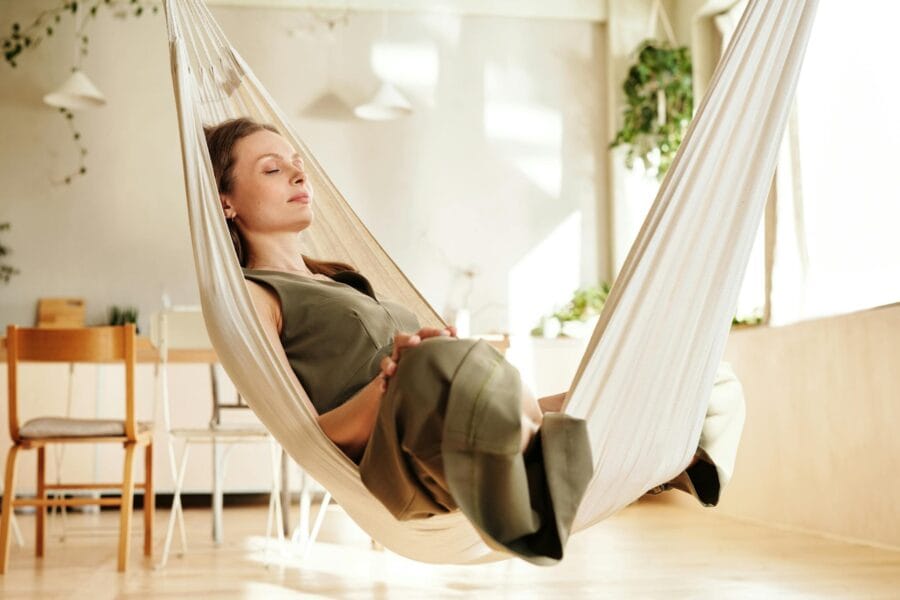 A woman enjoys a peaceful nap on an indoor hammock under soft natural light.