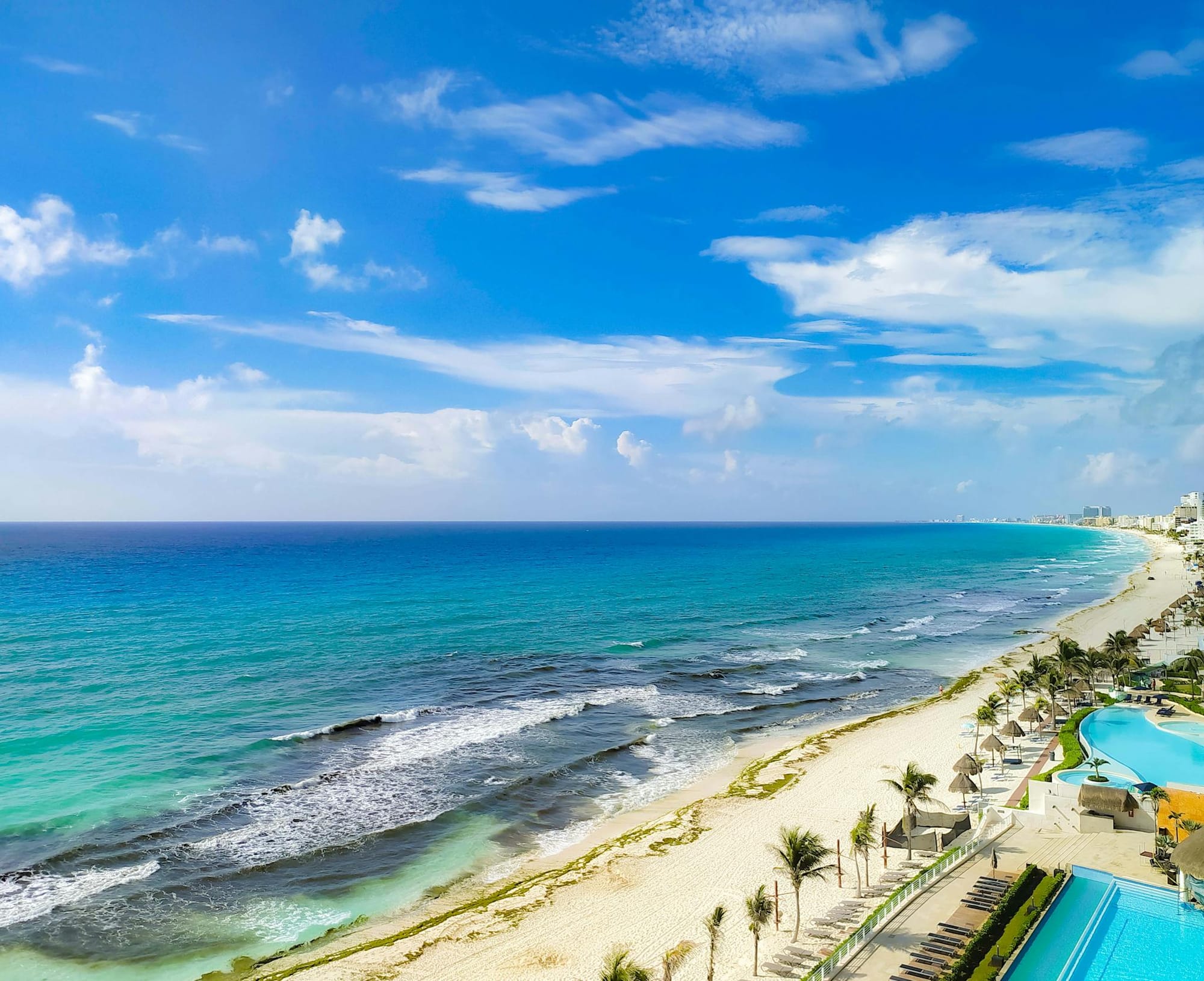 Aerial view of Cancún's coastline with turquoise sea, sandy beaches, and clear skies.