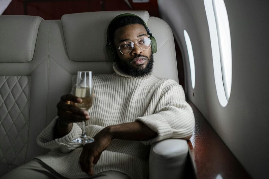 African American man relaxing in a private jet, sipping champagne and listening to music.