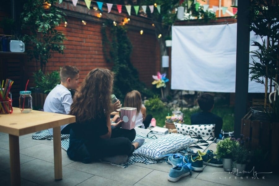 children sitting on pillows and blanket in backyard watching movie on screen