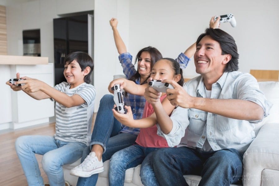 family sitting on couch having fun playing video games together