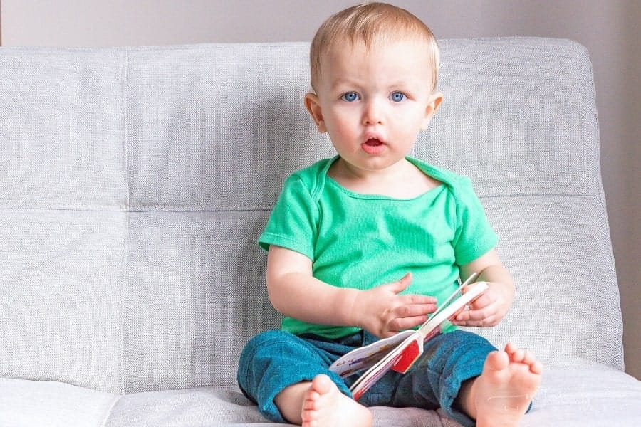 baby holding a board book and looking directly at the camera