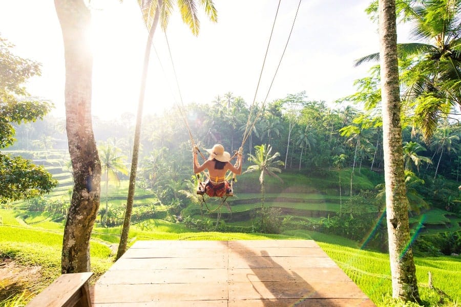 female tourist in Bali, Indonesia on a swing overlooking water