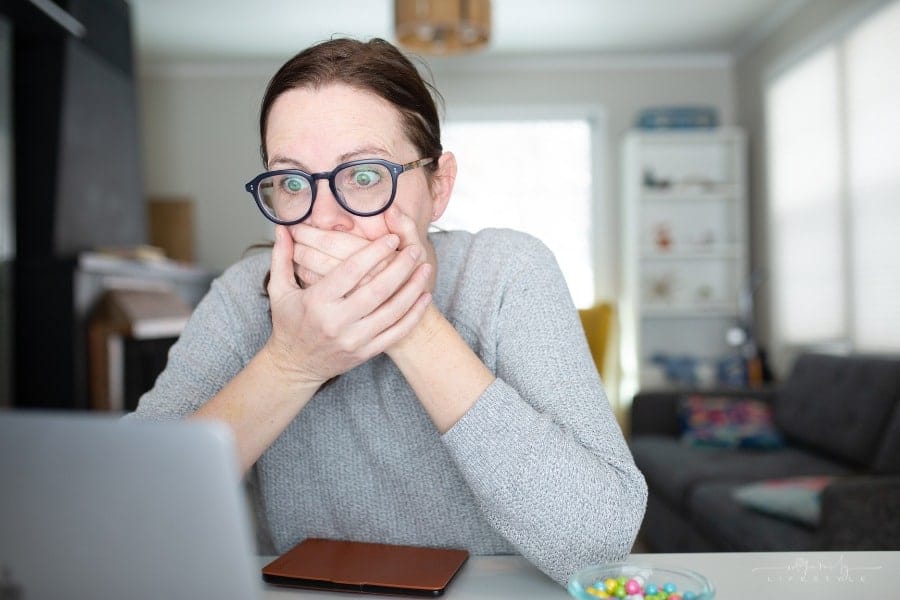 woman looking shocked and covering her mouth while looking at laptop