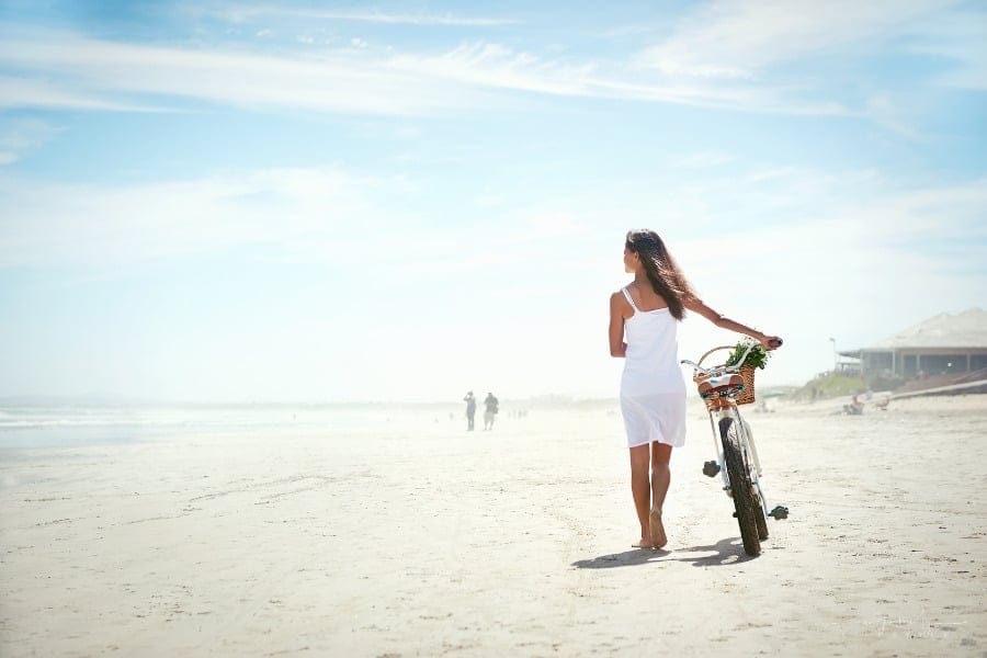 woman pushing a beach cruiser bike along a sandy beach