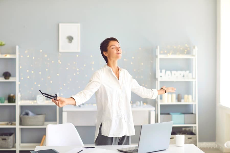 woman standing behind her desk with arms outstretched as she pratices breathing exercises