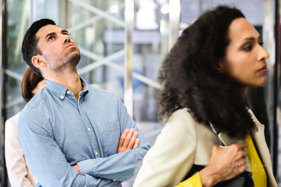 People waiting in line; annoyed man with arms crossed has his head thrown back and cheeks puffed with aggitation