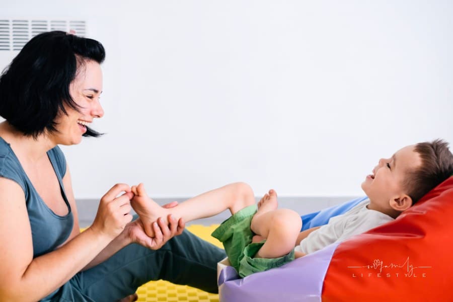 Mother playing with cute disabled child. Talking and communicating with cerebral palsy boy on the floor, mat, doing exercises