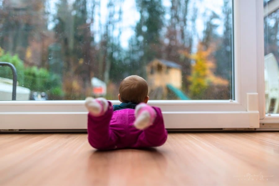Baby girl lying on wooden living room floor looking out the window door.