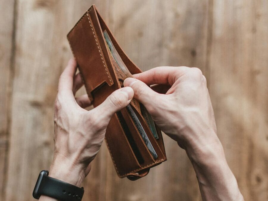 Close-up of hands holding a leather wallet with cash on a wooden background.