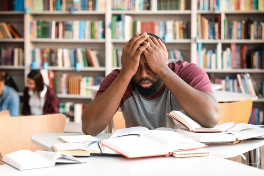 stressed male college student in school library with books open