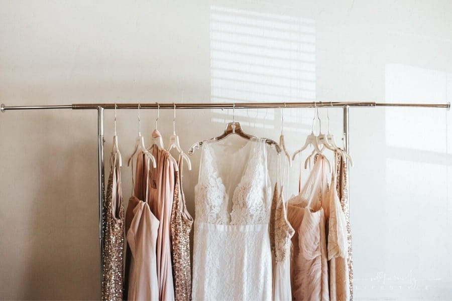 wedding gown surrounded by bridesmaid dresses all hanging from a clothing rod