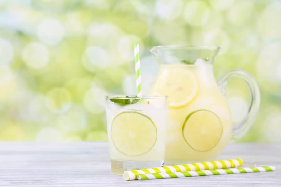 homemade lemonade in a glass and pitcher with lemon slices on a table