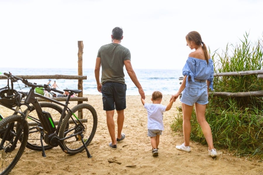 Family with toddler using e-bike in Tuscany entering beach, Italy