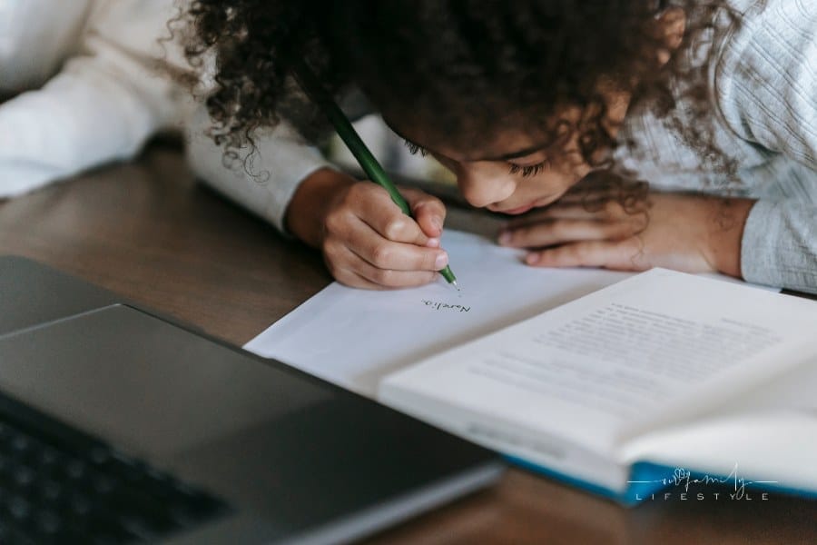 young girl writing on paper while reading book
