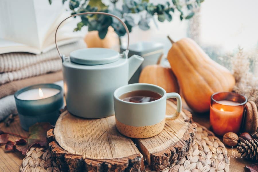 Cup and teapot in Scandinavian style on a wooden tray with gourds in background; cozy autumn aesthetic
