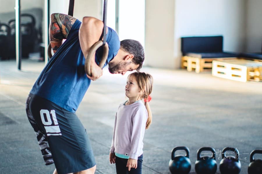 young father hanging on gymnastic rings while looking at his daughter