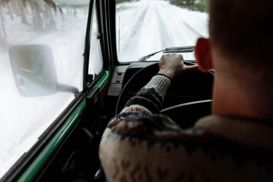 Experience driving on a snowy road with a person in a cozy sweater enjoying the winter view.