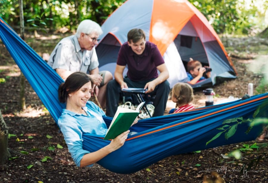 family camping in the forest with mom in hammock and grandpa and dad with kids