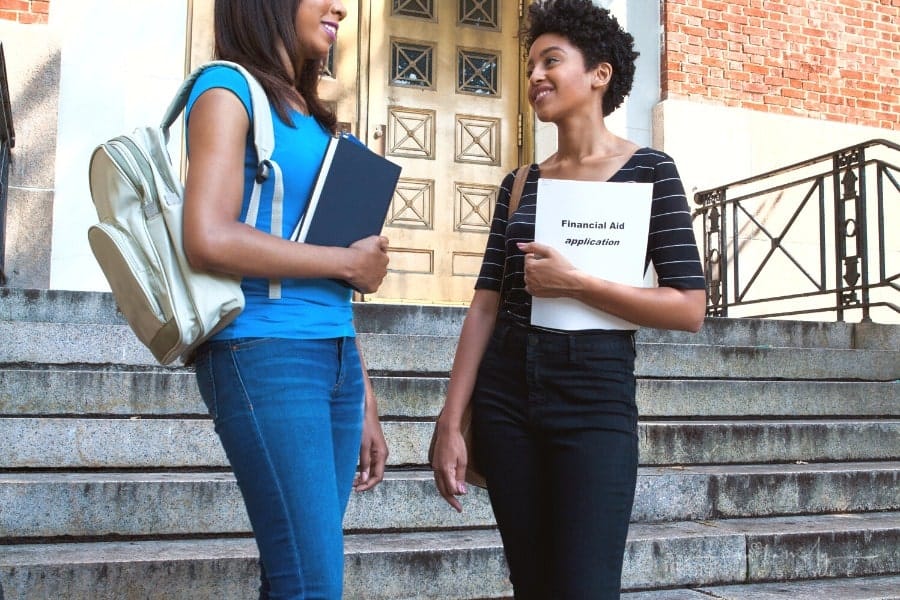 two students standing in front of building entrance with one holding financial aid application