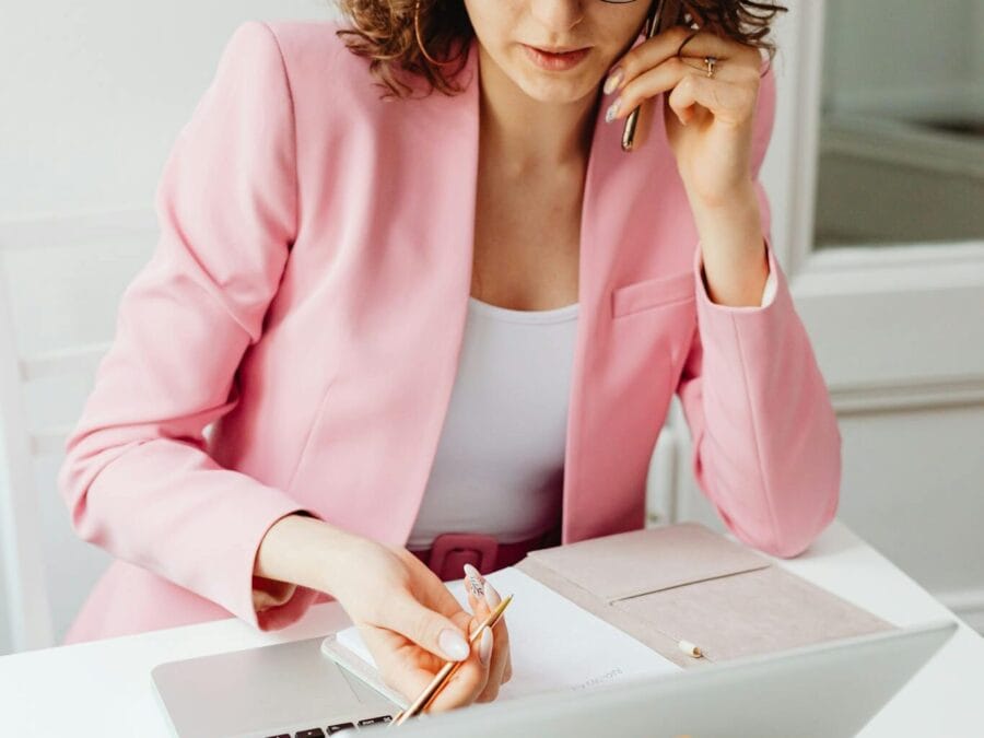 Focused woman in pink blazer working on laptop and phone.