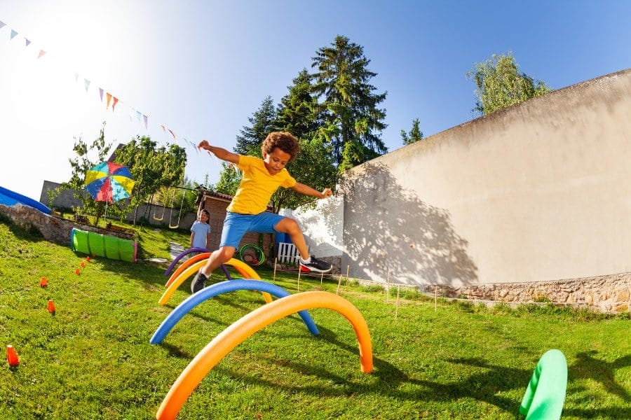 boy jumping over pool noodles being used as outdoor obstacle course