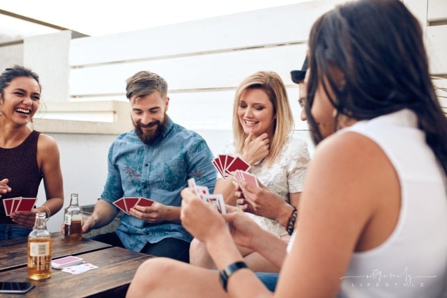 group of friends sitting at wooden table playing card game