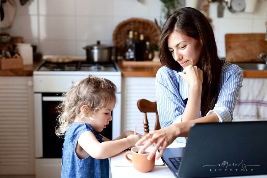 mom working on laptop smiling at daughter drawing nearby