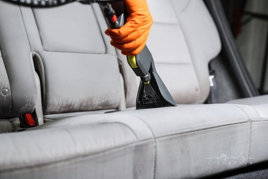 Close-up dry cleaning extractor machine is spraying water and detergent on textile seat inside car. Car dry cleaner is using
