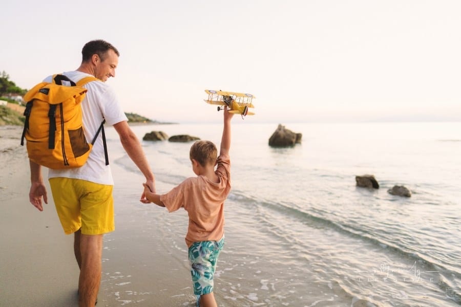 young boy with his dad playing with an airplane toy at the beach
