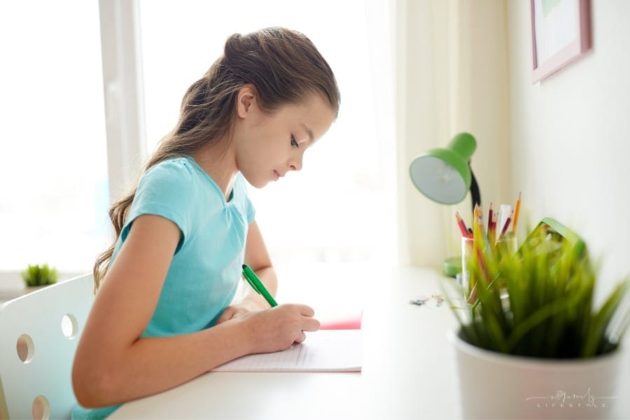 girl writing in a notebook at her bedroom desk