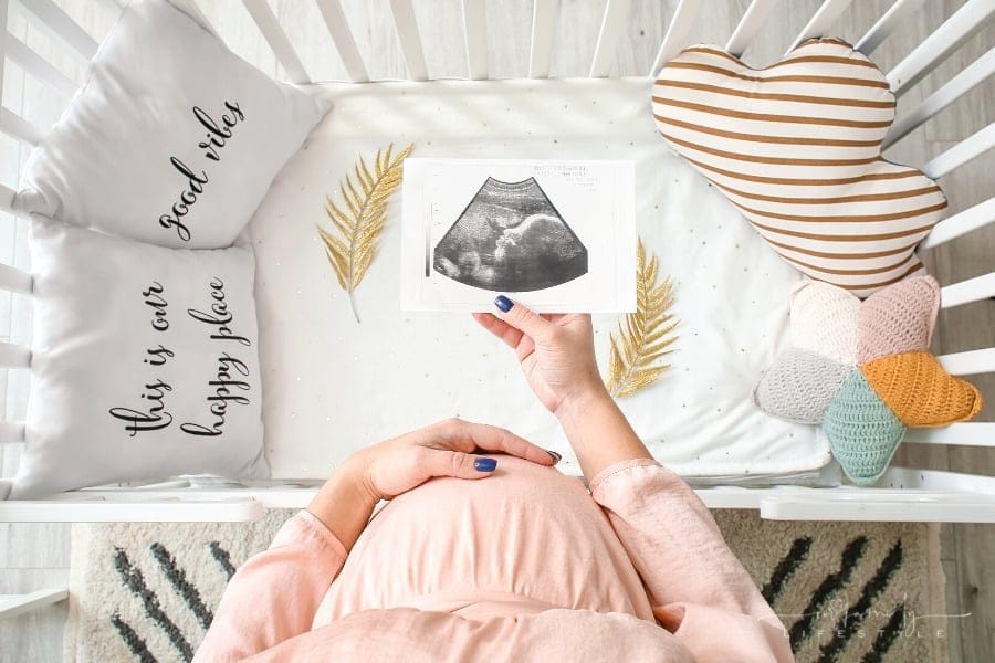 pregnant woman with one hand on stomach and other holding a sonogram over a crib