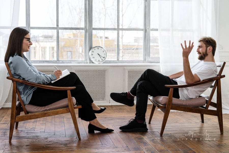 Person in Black Pants and Black Shoes Sitting on Brown Wooden Chair