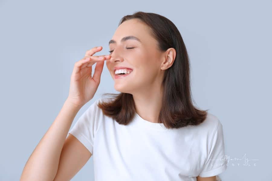 Young Happy Woman Touching Her Nose on Light Background, Closeup