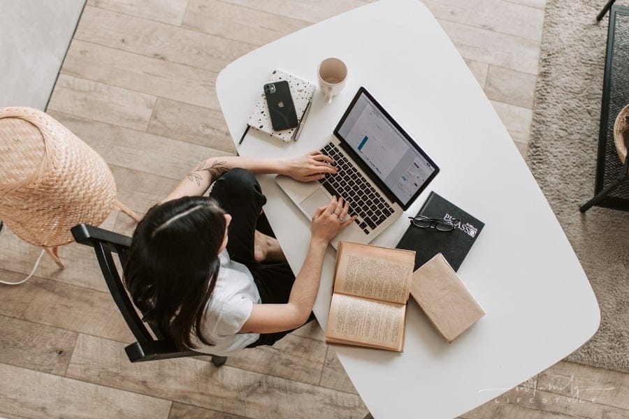 young woman typing on laptop surrounded by books on the desk
