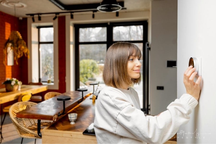 woman adjusting thermostat in kitchen of home