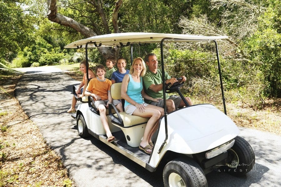 family riding on golf cart along tree-shadowed trail