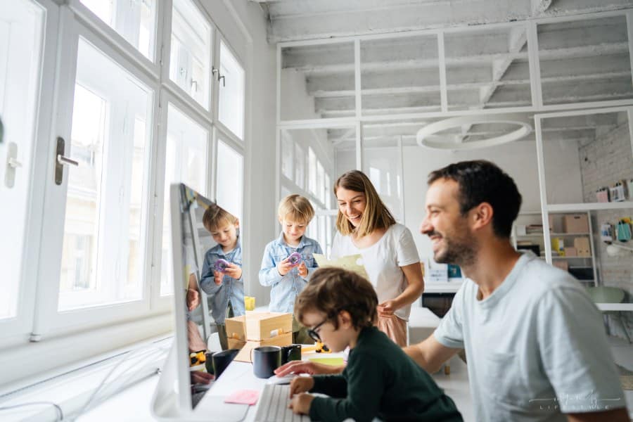 Photo of two young parents finishing work in their home-based office; accompanied by their two lovely sons; the daily routine