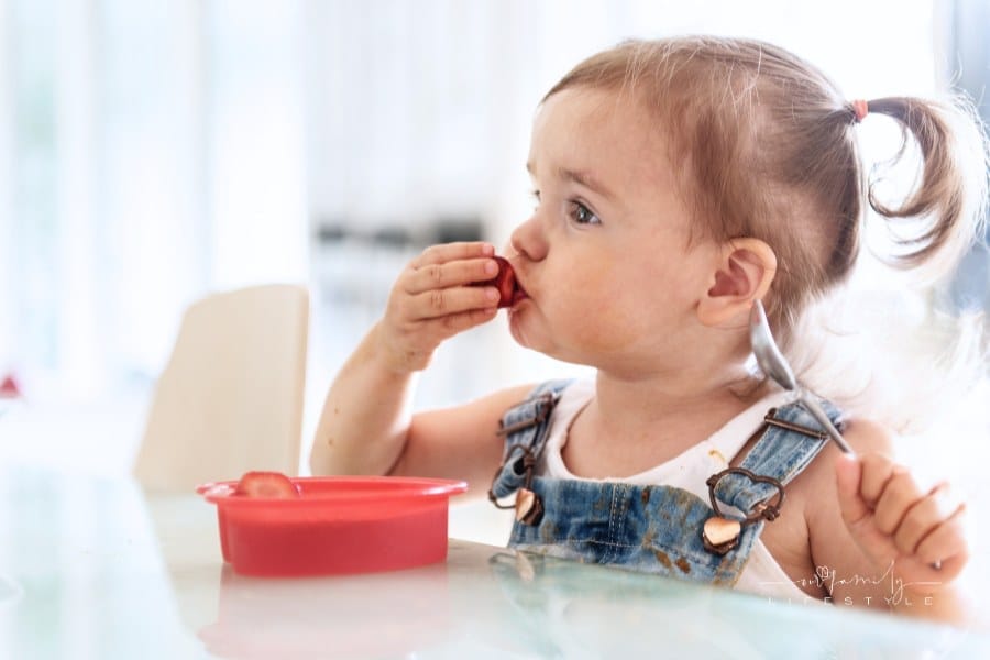 toddler girl eating strawberries at a table