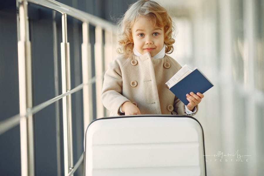 Child at the airport. Little girl with a suitcase. Girl in brown coat holding passport
